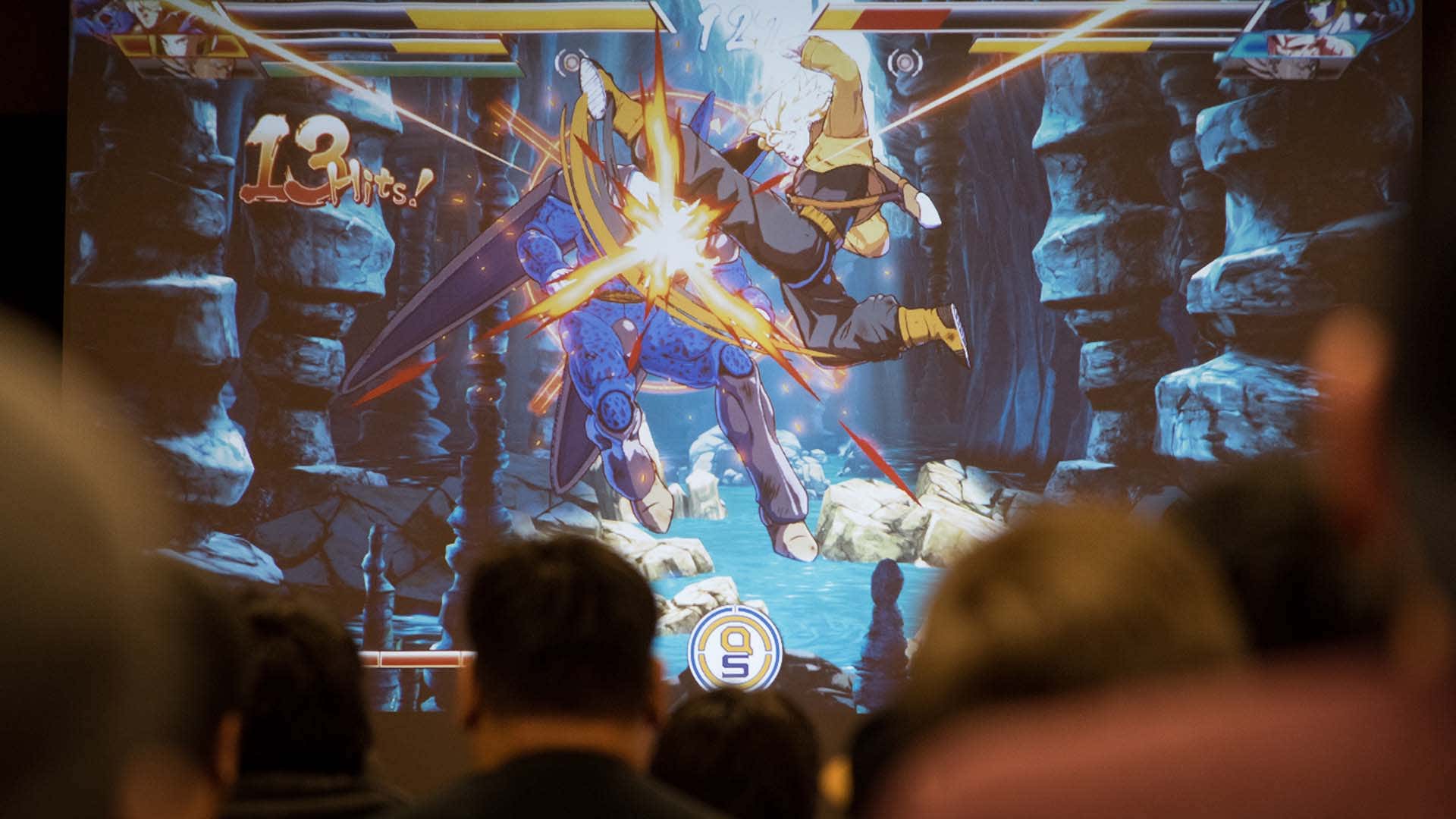 Ein Foto zeigt Menschen, die einen großen Bildschirm mit einem Kampfspiel darauf sehen. 